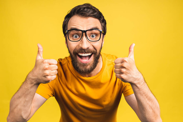 Happy young man. Portrait of handsome young bearded man smiling while standing isolated over yellow background. Thumbs up. - Φωτογραφία, εικόνα