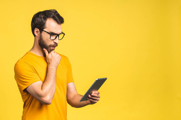 Amazed happy bearded man using digital tablet looking shocked about social media news, astonished man shopper consumer surprised excited by online win isolated over yellow background. - Фото, изображение