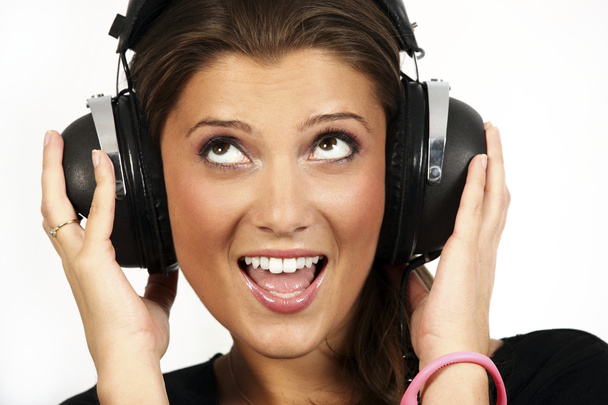A portrait of a beautiful girl listening to music on her big headphones over white background - Фото, изображение