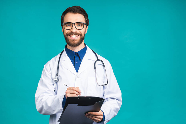 Happy smiling bearded doctor man writing recipe on clipboard, isolated over blue background. - Photo, image