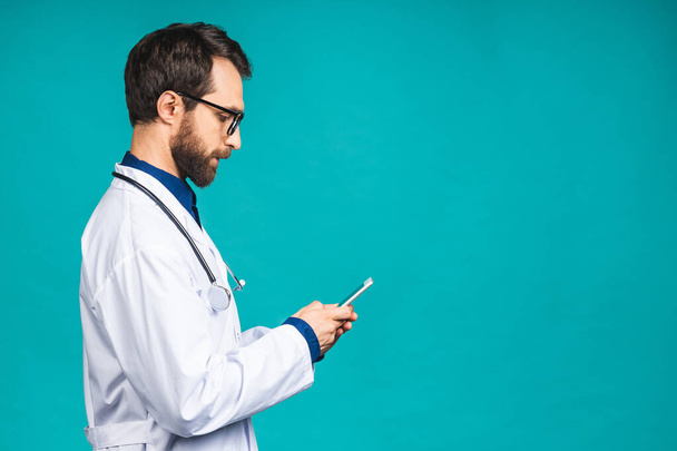 Young doctor texting on a smart phone isolated on a blue background. Using mobile phone.  - 写真・画像