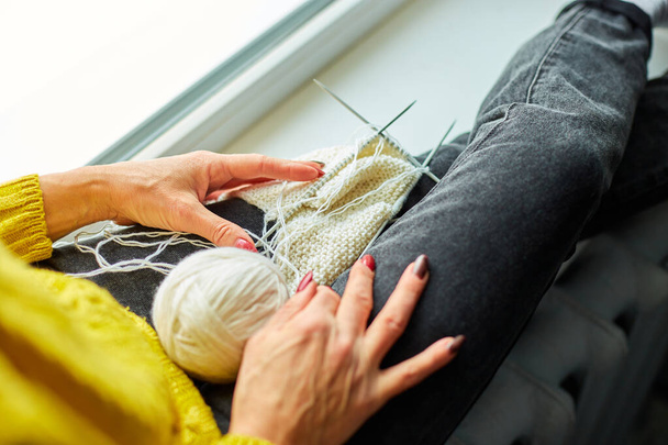 Mature female sitting on the windowsill and knitting while enjoying weekend at home, Senior woman knitting, relax at home do favorite hobby activity on weekend, wellbeing concept - Photo, Image