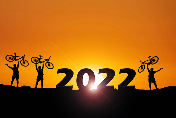 Σιλουέτες των 3 ανδρών με χαρά εκτρέφουν ποδήλατα το βράδυ. έννοια ευτυχισμένο το νέο έτος 2022 - Φωτογραφία, εικόνα