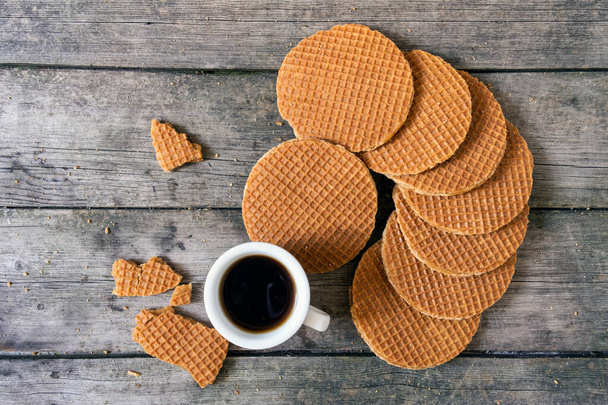 Geleneksel Hollanda waffleları karamel ve bir fincan kahve ile ahşap arka planda, üst manzara. - Fotoğraf, Görsel