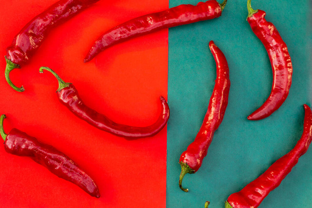 Κόκκινες καυτερές πιπεριές τσίλι διασκορπισμένες σε κόκκινο και σκούρο πράσινο φόντο - Φωτογραφία, εικόνα
