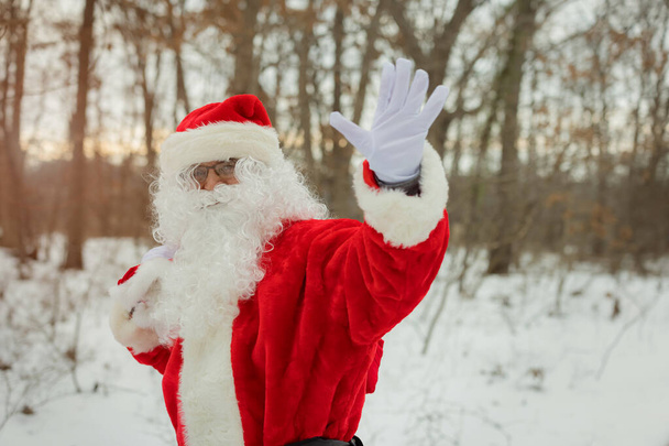 Nieve Santa Claus caminando por la calle lleva una gran bolsa de regalos en los árboles cubiertos de nieve - Foto, imagen