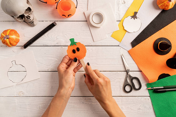 Happy Halloween concept. Step by step instruction of making halloween bookmark DIY pumpkin craft. Step 6 - stick a pumpkin and the ice cream stick. Bookmark is ready. Top view flat lay - Zdjęcie, obraz