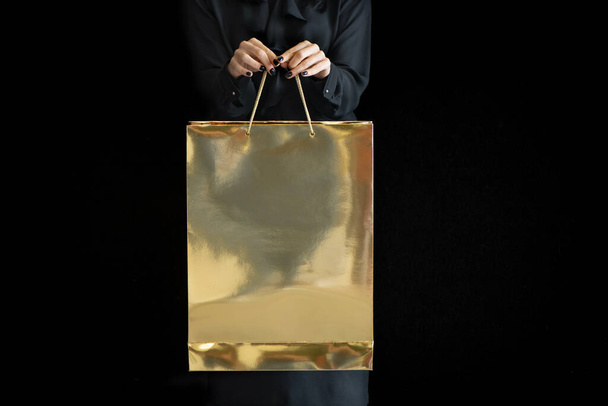 Unerkennbare Frau mit goldener Einkaufstasche auf dunklem Hintergrund. - Foto, Bild