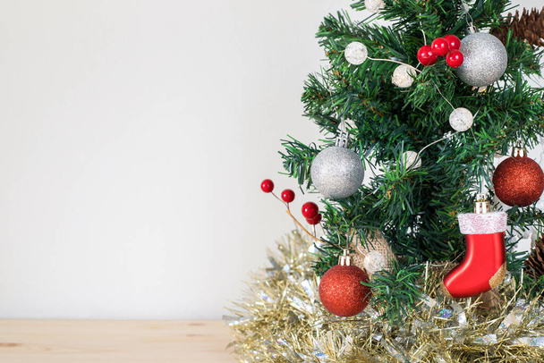 Рождественская елка с украшениями на деревянном столе и белом фоне стены с копировальным пространством для текста - Фото, изображение