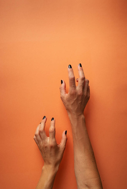 Gelukkig Halloween concept. Griezelige vrouw Halloween handen met zwarte nagels op oranje achtergrond - Foto, afbeelding