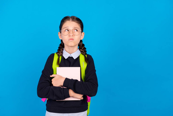 Photo of unhappy upset negative mood look copyspace grimace hold book wear backpack isolated on blue color background - Foto, afbeelding