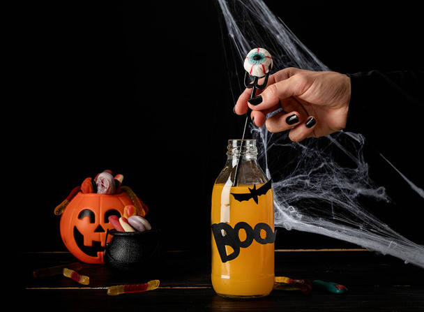 Gelukkig Halloween concept. vrouw hand met zwarte nagels houden eng kleurrijke Halloween cocktail met feest decoraties op donkere achtergrond - Foto, afbeelding