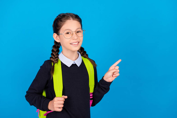 Photo of cheerful good mood schoolgirl point finger copyspace advertise product isolated on blue color background - Zdjęcie, obraz