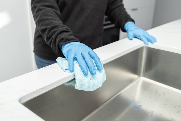 Ręce w rękawicy ochronnej czyszczącej nowoczesny zlew z szmatą minimalistycznej kuchni domowej - Zdjęcie, obraz