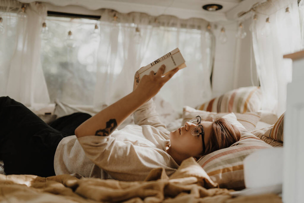 Beautiful woman reading book in a camper van. - Fotó, kép