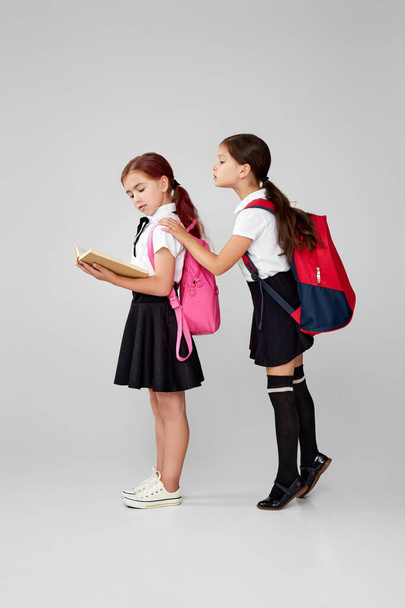 two little cheerful friends schoolgirls with backpacks read book - Fotó, kép