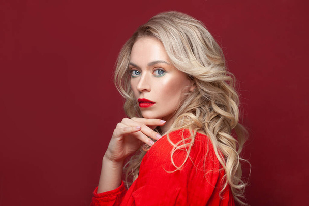 Femme modèle blonde mature élégante avec maquillage des lèvres rouges et cheveux bouclés sains sur fond de bannière rouge, portrait - Photo, image
