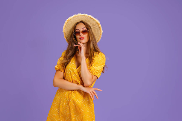 Portrait of excited young woman in yellow dress, summer hat, sunglasses posing isolated on pastel violet background. - Fotografie, Obrázek