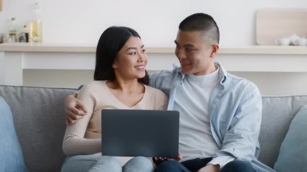 Vrolijk Koreaans paar met behulp van laptop computer samen zitten thuis - Video