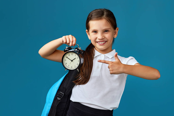 schoolgirl with backpack is holding alarm clock - Foto, Bild