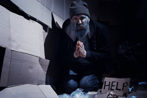 Evsiz sakallı bir adam sokakta kutulara oturup yardım istiyor. Evsiz bir insan yemek için para ister ve bir gecede. - Fotoğraf, Görsel