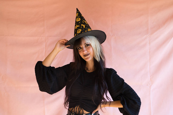 mladá žena s blond a hnědé vlasy oblečené jako čarodějnice na halloween party. Má na sobě čarodějnický klobouk a černé šaty.. - Fotografie, Obrázek