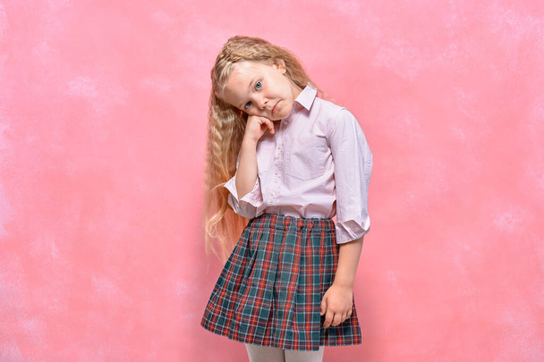 sad pensive little girl. schoolgirl in uniform. pink background - Foto, imagen
