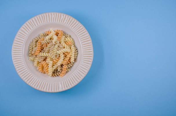 Un plato con torceduras de pasta aisladas sobre un fondo azul con espacio libre para el texto - Foto, Imagen