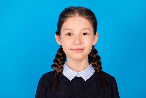 Portrait of young pretty charming good mood peaceful schoolgirl with two braids isolated on blue color background - 写真・画像