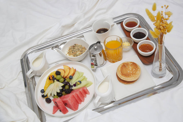 豪華なリゾートのベッドでの朝食トレイ。トレイ上の果物、パンケーキ、シリアル、コーヒーとジュースでベッドで朝食。. - 写真・画像