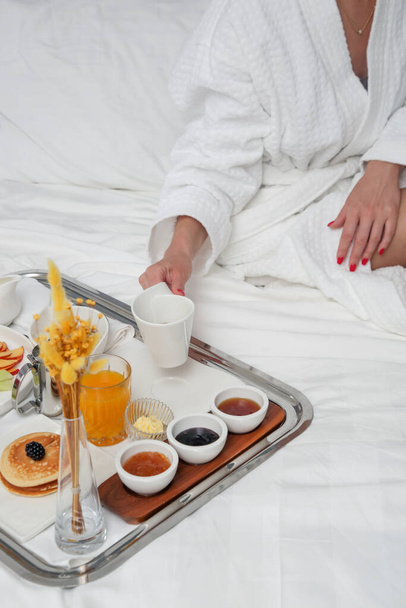 Breakfast tray in bed in luxury resort. Breakfast in bed with fruits, pancakes, cereals, coffee and juice on a tray. - Photo, Image