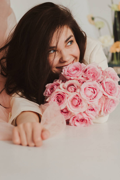 Closeup of a beautiful happy bride in jacket smiling and holding a rose bouquet - Zdjęcie, obraz
