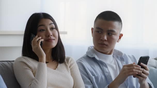 Geloso asiatico marito guardando moglie parlando su telefono indoor - Filmati, video