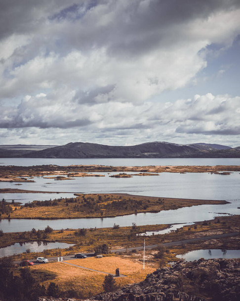 A vertical shot of a lake surrounded by hills under a cloudy sky in Thingvellir National Park, Iceland - Photo, image