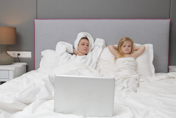 Мама та її маленька дівчинка дивляться мультфільми на ноутбуці в ліжку. - Фото, зображення