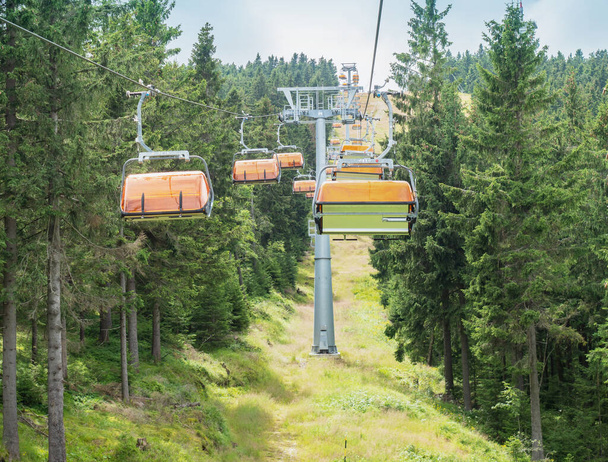 Chairlift com cobertura de vento laranja de assentos tremendo no caminho para cima através da floresta. A bicicleta downhill única pista abaixo elevador. - Foto, Imagem