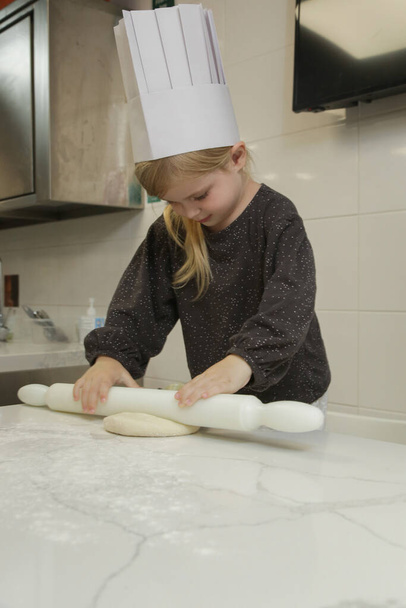 Ένα μικρό κοριτσάκι μαθαίνει να βγάζει λεφτά στο μάθημα μαγειρικής. Τάξη ζαχαροπλαστικής με μικρά παιδιά σεφ. - Φωτογραφία, εικόνα