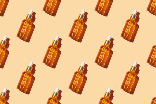 Seamless pattern of serum in glass bottle with dropper on pastel orange background. - Photo, image
