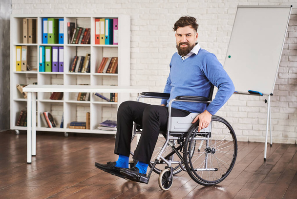 Lächelnder behinderter Geschäftsmann sitzt im Rollstuhl in seinem Büro - Foto, Bild