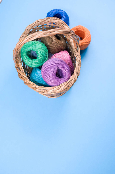 A vertical shot of colored cotton threads in a basket on a blue background - Foto, Bild