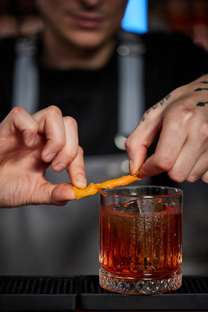 bartender makes a cocktail in a glass with orange peel - Foto, afbeelding