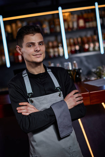 Handsome barman in apron standing at the bar counter - Фото, изображение