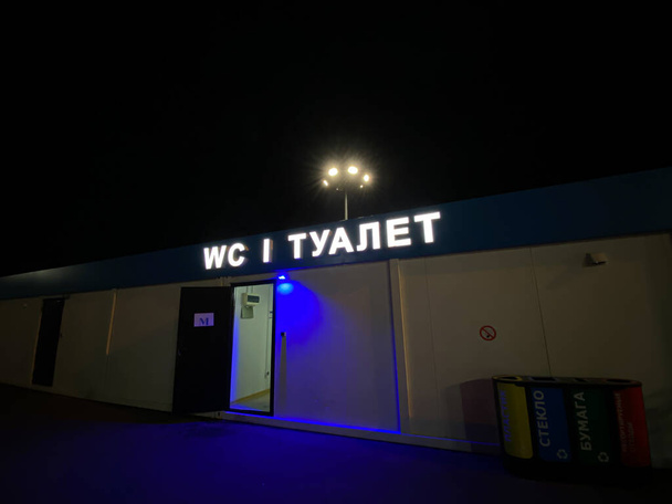 Una inscripción brillante en ruso - WC. Entrada al WC público. Noche oscura - Foto, Imagen