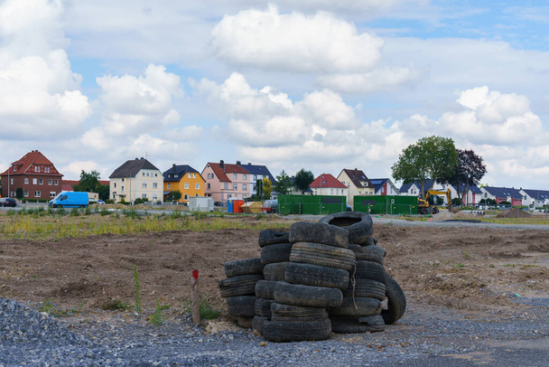 Un mucchio di pneumatici per auto usate si trova in un terreno vuoto. Sullo sfondo ci sono case residenziali sotto un cielo nuvoloso. - Foto, immagini