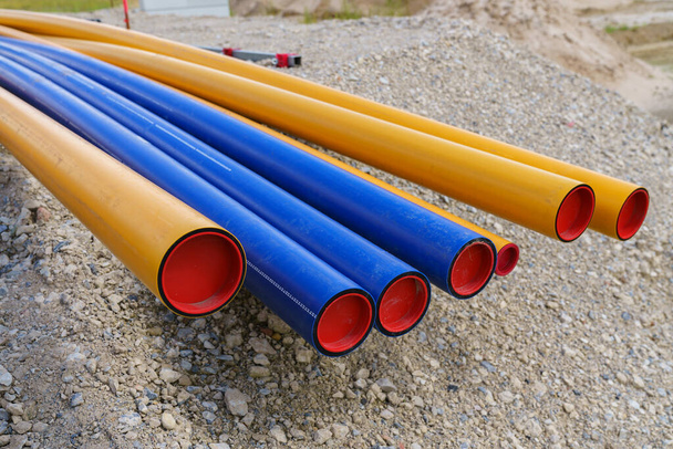 Site de construction. Des piles de tuyaux électriques en PVC orange-jaune et bleu se trouvent sur le gravier.. - Photo, image