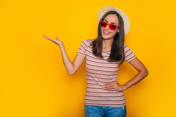 Happy excited beautiful tourist woman in hat and sunglasses is posing on yellow background and having fun - Fotó, kép