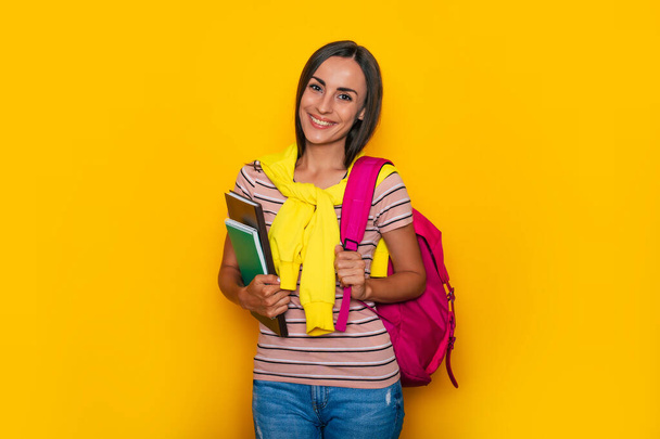Happy cute student girl in modern casual clothes with pink backpack is posing in studio - Zdjęcie, obraz