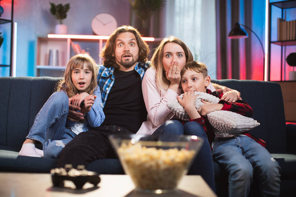 Scared parents with kids watching horror movie at home - Foto, afbeelding