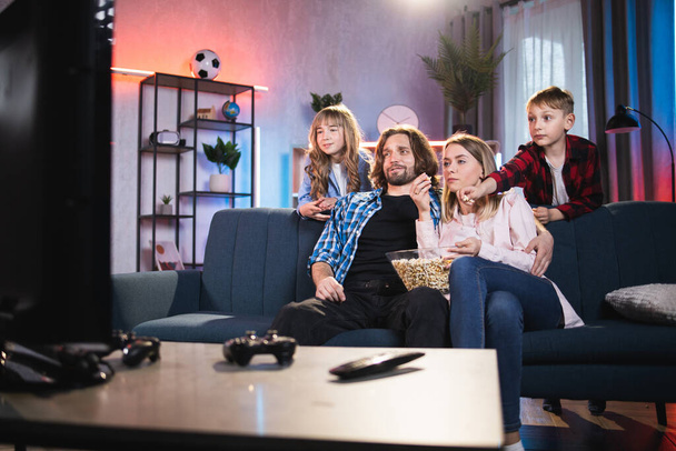 Los padres y sus dos niños lindos niño y niña, viendo el programa de televisión en casa - Foto, Imagen