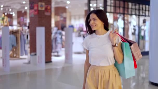Mujer feliz dejando la tienda en el centro comercial con muchas bolsas de papel llenas de compras - Metraje, vídeo